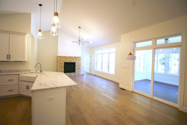 kitchen featuring light stone counters, vaulted ceiling, sink, a fireplace, and white cabinetry