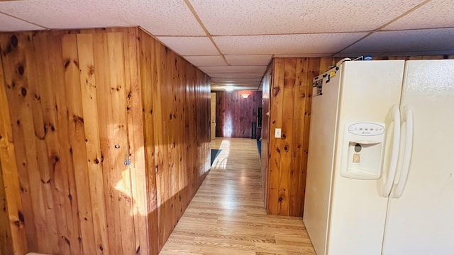 hall featuring wooden walls, a drop ceiling, and light hardwood / wood-style floors