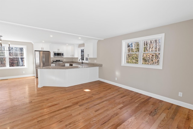 kitchen featuring kitchen peninsula, appliances with stainless steel finishes, light wood-type flooring, sink, and white cabinetry