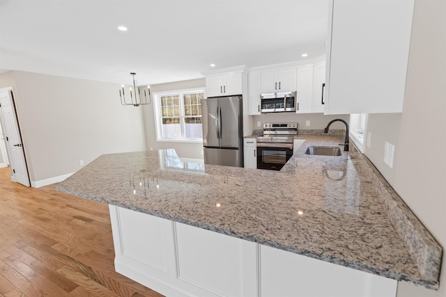 kitchen featuring kitchen peninsula, appliances with stainless steel finishes, light stone counters, sink, and white cabinetry