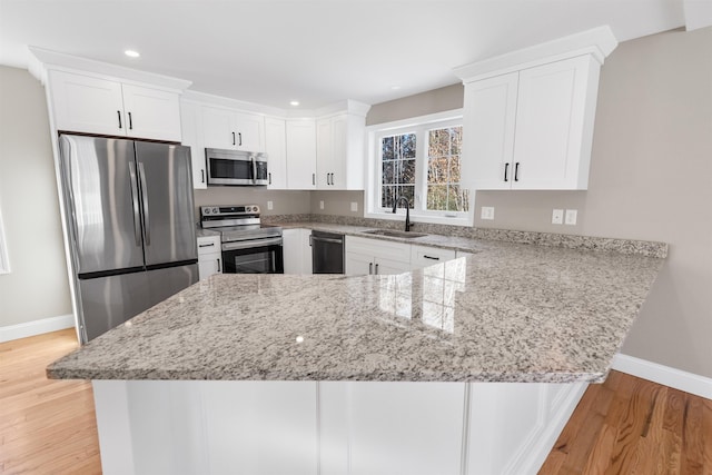 kitchen with kitchen peninsula, appliances with stainless steel finishes, light stone counters, sink, and white cabinetry