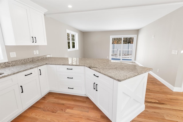 kitchen with light stone countertops, white cabinetry, and kitchen peninsula