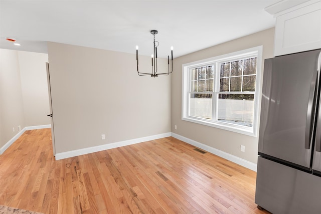 unfurnished dining area featuring light wood-type flooring and a chandelier