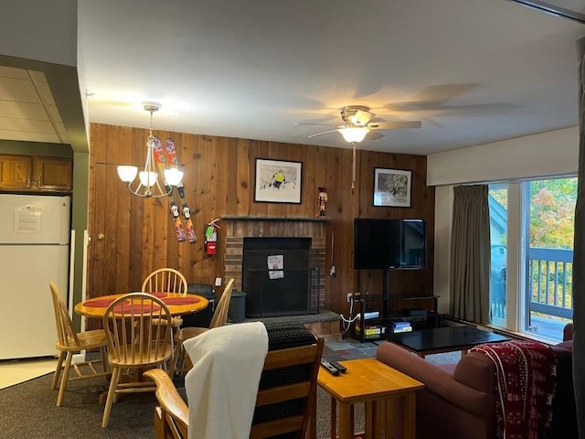 living room featuring ceiling fan with notable chandelier, a brick fireplace, and wooden walls