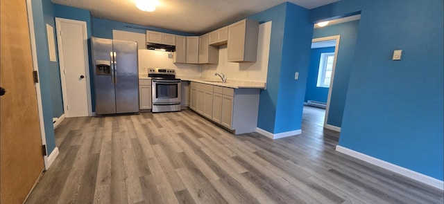 kitchen with wood-type flooring, sink, a textured ceiling, stainless steel appliances, and baseboard heating