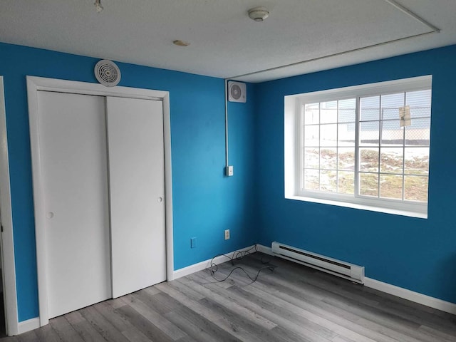 unfurnished bedroom featuring a baseboard heating unit, a closet, and light wood-type flooring