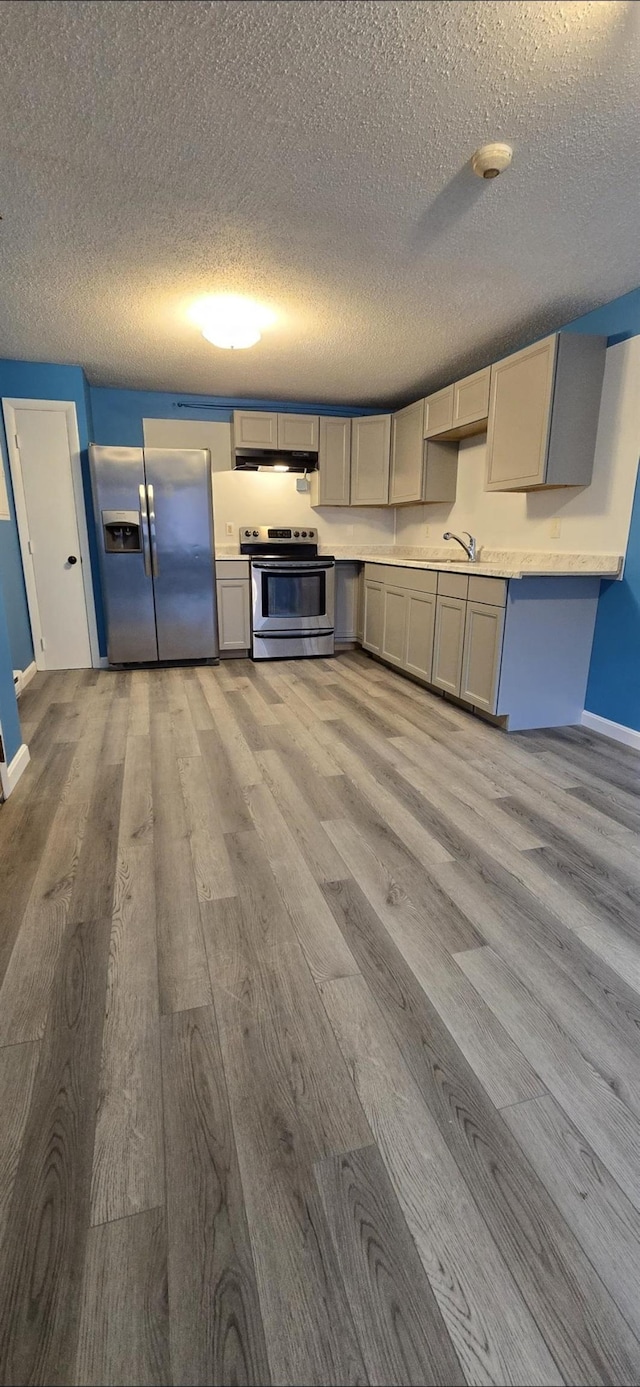 kitchen featuring appliances with stainless steel finishes, light hardwood / wood-style floors, gray cabinetry, and a textured ceiling