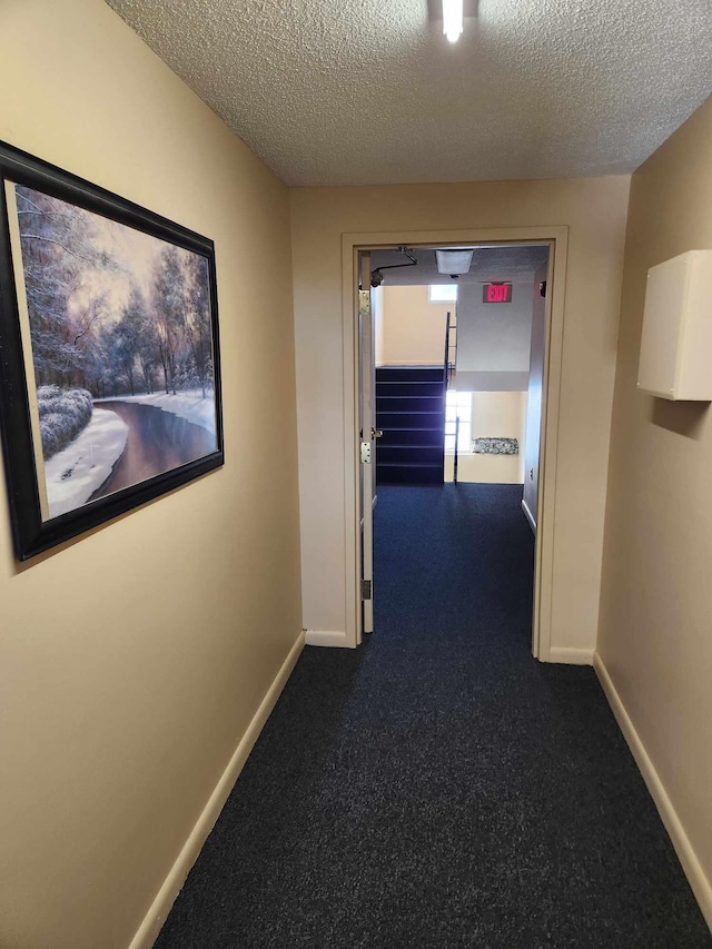 hallway featuring dark carpet and a textured ceiling