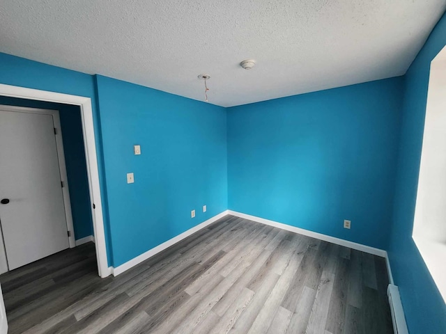 empty room with a textured ceiling, a baseboard heating unit, and hardwood / wood-style floors