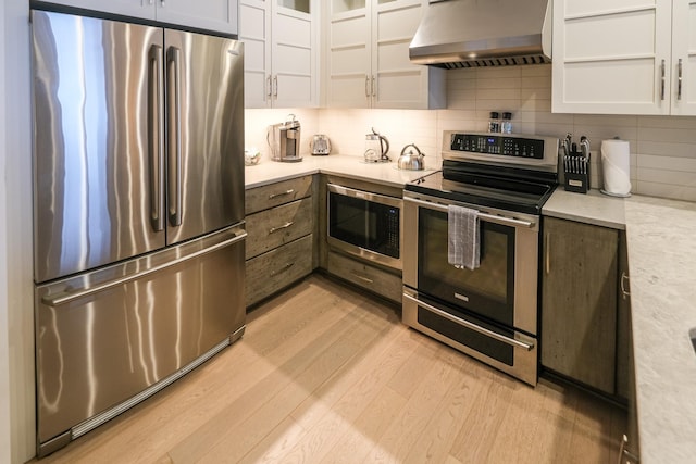 kitchen featuring stainless steel appliances, light hardwood / wood-style floors, wall chimney range hood, and white cabinets