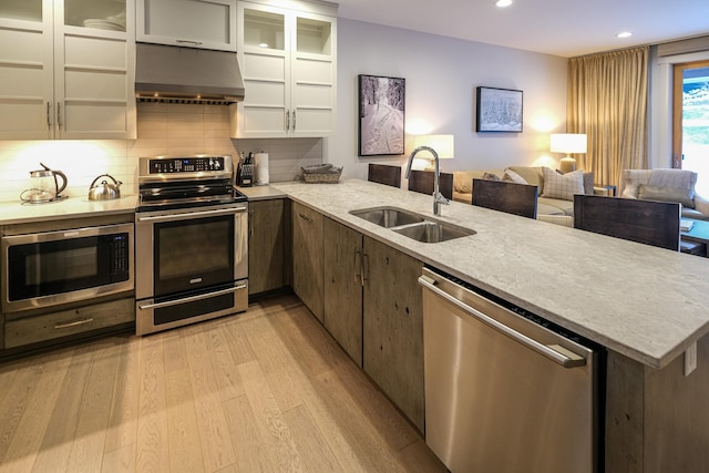 kitchen with appliances with stainless steel finishes, range hood, white cabinetry, sink, and light hardwood / wood-style floors