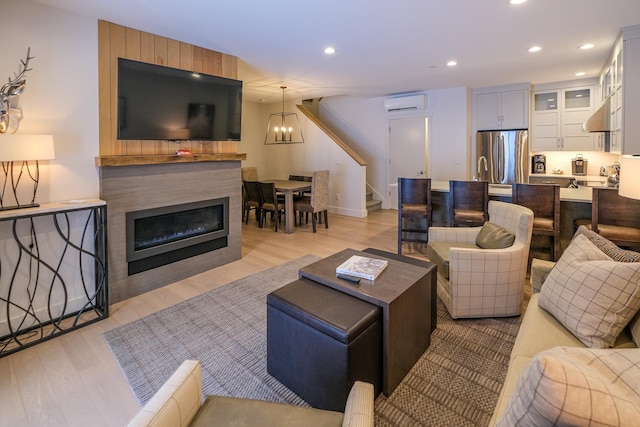 living room featuring an inviting chandelier, a wall mounted air conditioner, and light hardwood / wood-style flooring