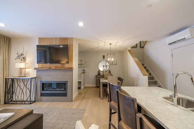 kitchen with decorative light fixtures, sink, a kitchen breakfast bar, a wall unit AC, and light hardwood / wood-style flooring