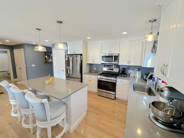 kitchen featuring pendant lighting, sink, appliances with stainless steel finishes, a kitchen island, and white cabinetry