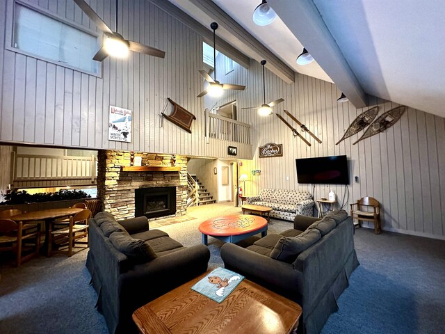 living area featuring a stone fireplace, carpet floors, beam ceiling, and a ceiling fan