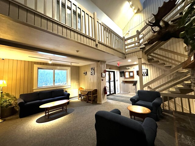 living room with stairway, carpet floors, a high ceiling, wood walls, and baseboard heating