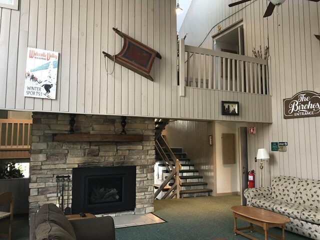 carpeted living room featuring stairway, a stone fireplace, and a ceiling fan