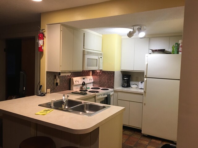 kitchen with tasteful backsplash, light countertops, a peninsula, white appliances, and a sink