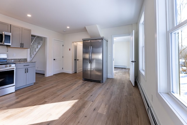 kitchen with baseboard heating, gray cabinets, light stone counters, and appliances with stainless steel finishes