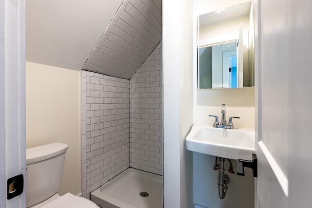 bathroom with a tile shower, sink, vaulted ceiling, and toilet