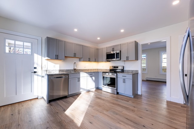 kitchen featuring stone counters, sink, appliances with stainless steel finishes, and a baseboard heating unit