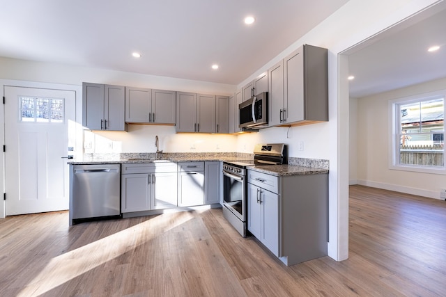 kitchen with sink, light hardwood / wood-style flooring, dark stone counters, gray cabinets, and appliances with stainless steel finishes