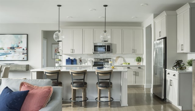 kitchen with decorative light fixtures, white cabinetry, stainless steel appliances, and an island with sink