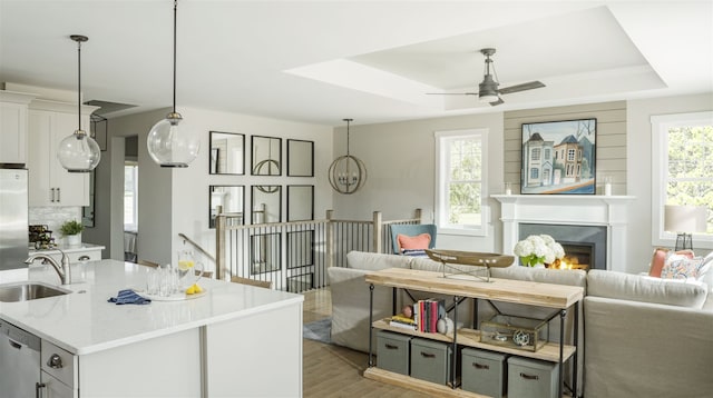 kitchen with light stone countertops, appliances with stainless steel finishes, a tray ceiling, sink, and light hardwood / wood-style floors