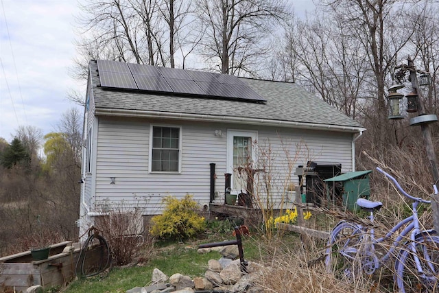 rear view of property with roof with shingles and solar panels