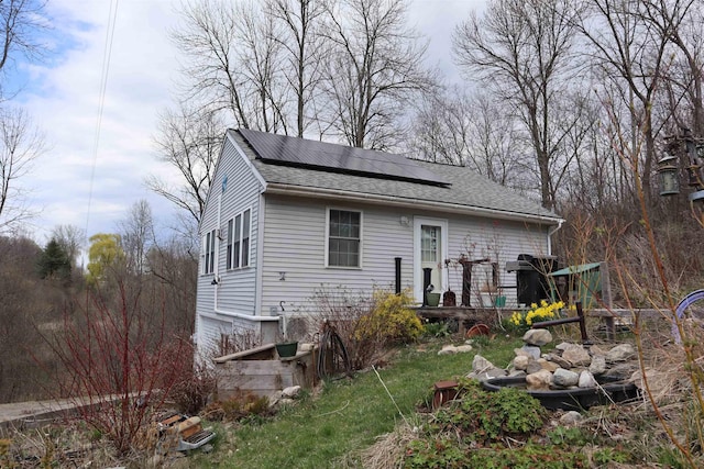 rear view of property with solar panels, a deck, and a shingled roof