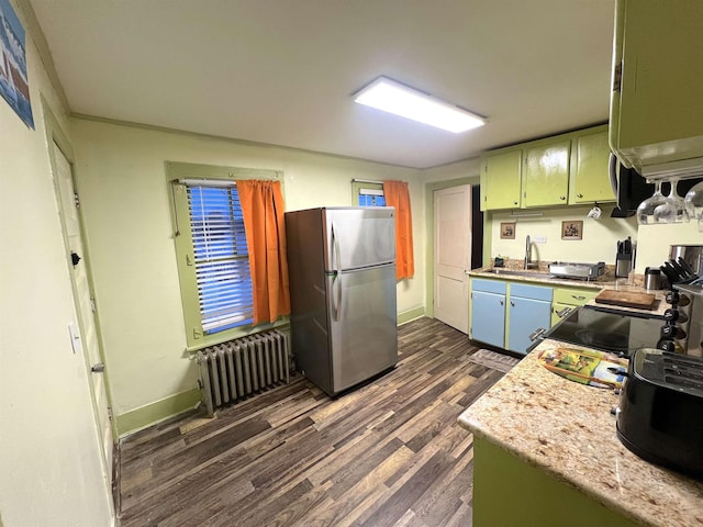 kitchen with stainless steel fridge, light stone counters, radiator, sink, and dark hardwood / wood-style floors