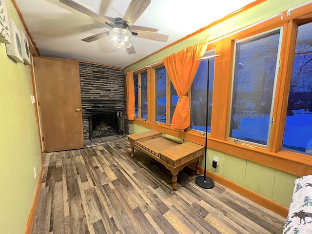 interior space featuring hardwood / wood-style flooring, ceiling fan, a large fireplace, and crown molding