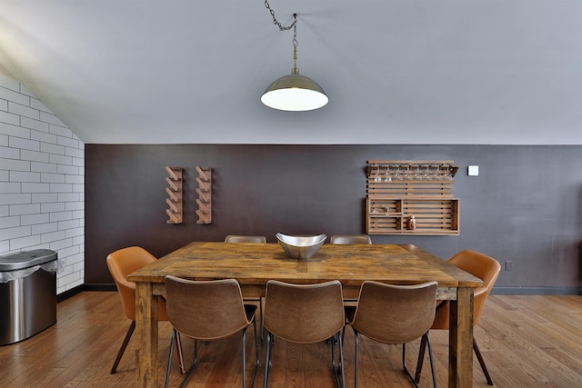 dining room featuring hardwood / wood-style floors, lofted ceiling, and brick wall