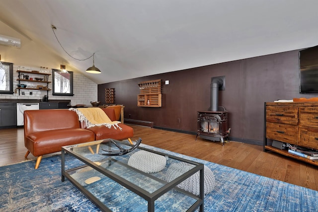 living room with hardwood / wood-style floors, vaulted ceiling, a wood stove, and a baseboard heating unit