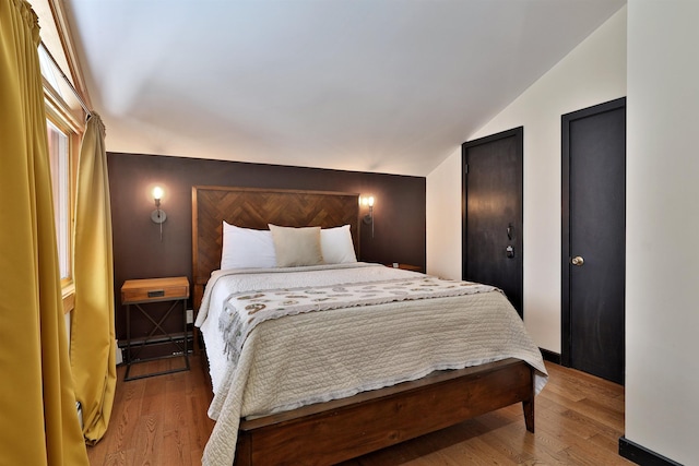 bedroom with hardwood / wood-style flooring, a baseboard radiator, and lofted ceiling