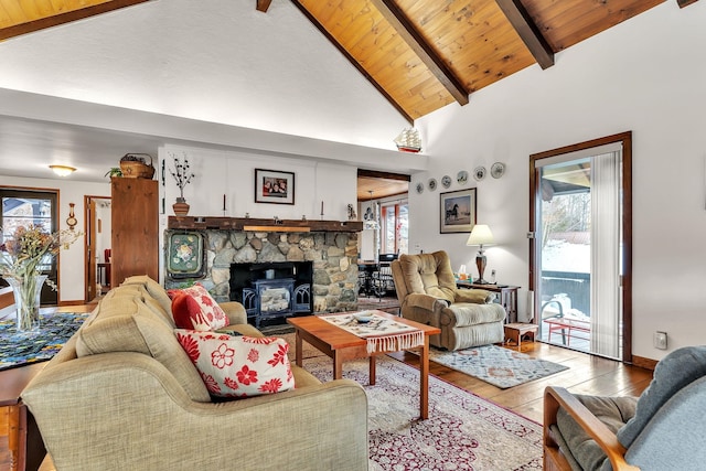 living room featuring beamed ceiling, light hardwood / wood-style floors, a wood stove, and a healthy amount of sunlight