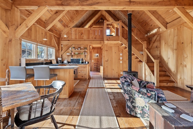 kitchen with wooden walls, high vaulted ceiling, a kitchen island, beamed ceiling, and light wood-type flooring