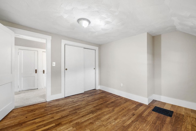 unfurnished bedroom with a textured ceiling, hardwood / wood-style flooring, a closet, and lofted ceiling