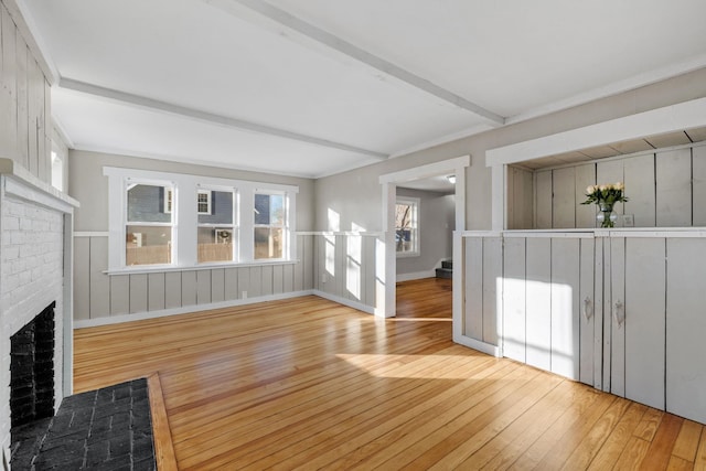 unfurnished living room featuring beam ceiling, a brick fireplace, and light wood-type flooring