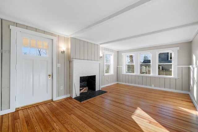 unfurnished living room with a fireplace, light hardwood / wood-style floors, and beamed ceiling