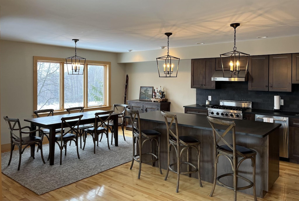 kitchen with dishwasher, a kitchen breakfast bar, stove, decorative light fixtures, and dark brown cabinets