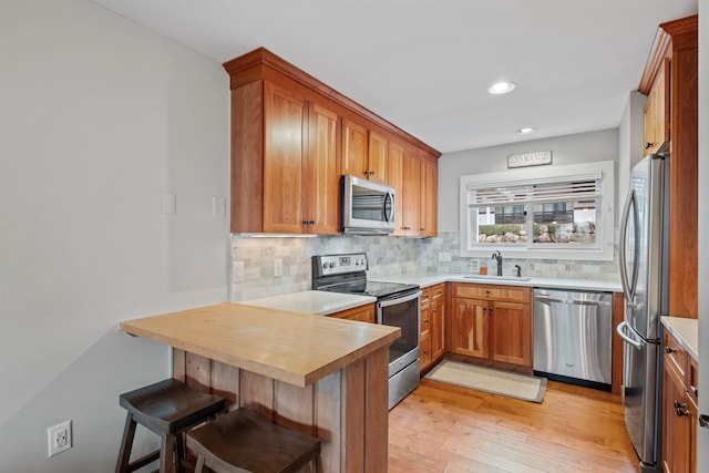 kitchen featuring kitchen peninsula, a kitchen breakfast bar, tasteful backsplash, stainless steel appliances, and sink