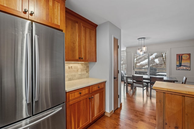 kitchen with pendant lighting, backsplash, stainless steel refrigerator, and light hardwood / wood-style flooring