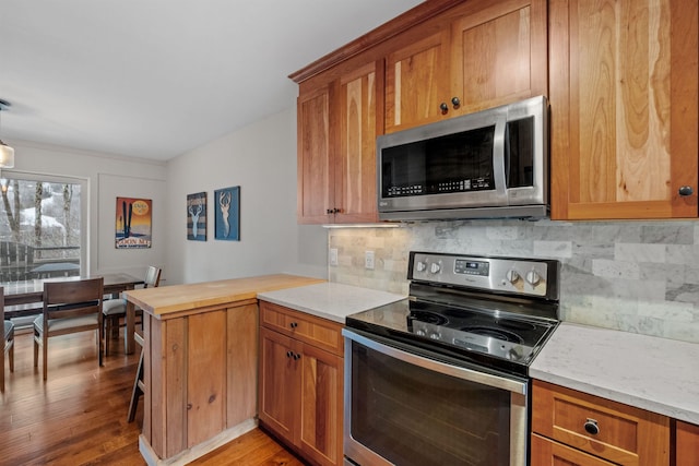 kitchen featuring backsplash, kitchen peninsula, decorative light fixtures, appliances with stainless steel finishes, and light wood-type flooring