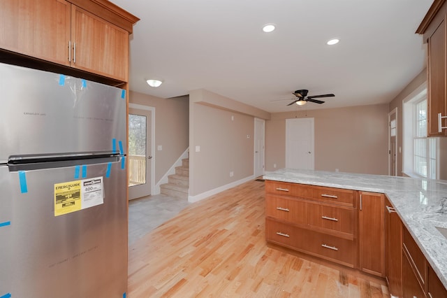 kitchen featuring ceiling fan, light stone counters, stainless steel refrigerator, and light hardwood / wood-style flooring