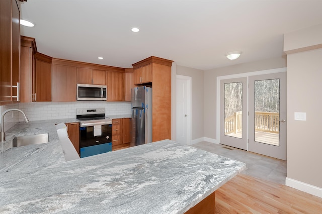 kitchen with sink, tasteful backsplash, light stone counters, kitchen peninsula, and appliances with stainless steel finishes