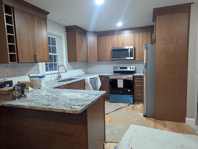 kitchen with light stone countertops, sink, tasteful backsplash, kitchen peninsula, and appliances with stainless steel finishes