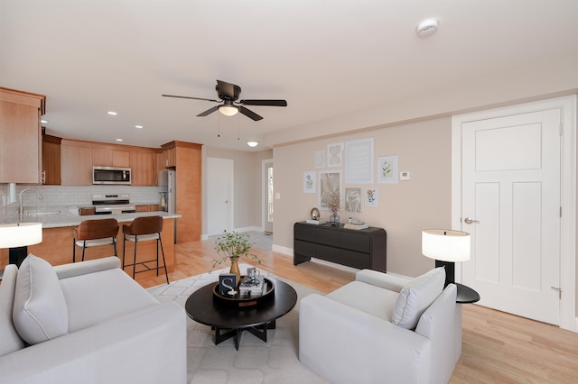 living room with ceiling fan, sink, and light wood-type flooring