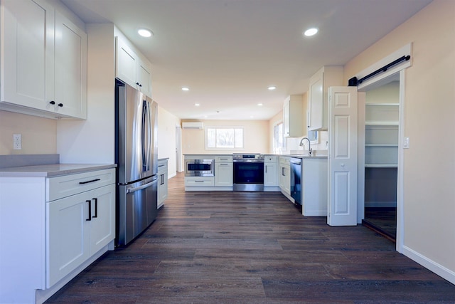 kitchen featuring white cabinets, sink, dark hardwood / wood-style floors, a barn door, and appliances with stainless steel finishes