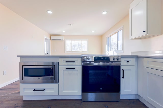 kitchen with white cabinets, stainless steel appliances, a wall mounted air conditioner, and dark wood-type flooring